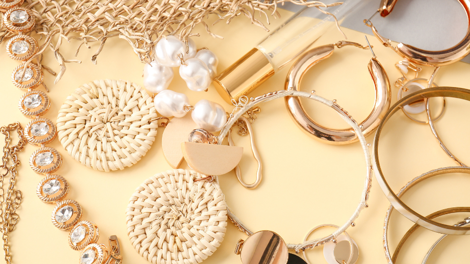 A stylish assortment of jewelry and accessories, including woven earrings, gold hoops, and pearl accents, displayed on a light background.