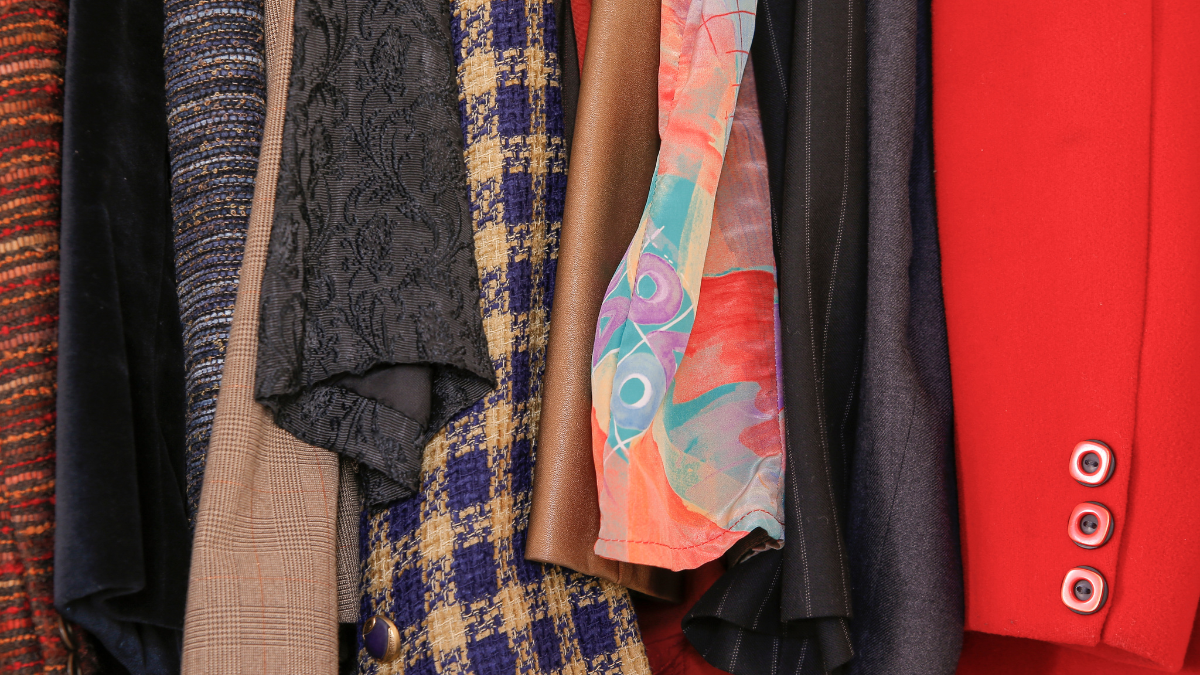 A collection of vibrant and textured fabrics, featuring a mix of patterns and colours, hanging neatly in a wardrobe.