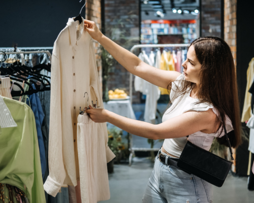 A woman examines a white blouse in a clothing store, carefully considering her options among the racks of colourful garments.