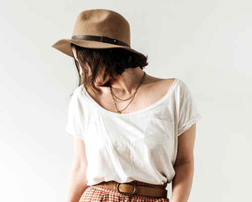 A woman wearing a white t-shirt, patterned pants, and a brown hat poses stylishly, showcasing a relaxed and fashionable look.