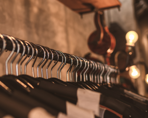 A row of metal hangers holding garments, set against a rustic backdrop with warm lighting, creates a stylish and industrial display.